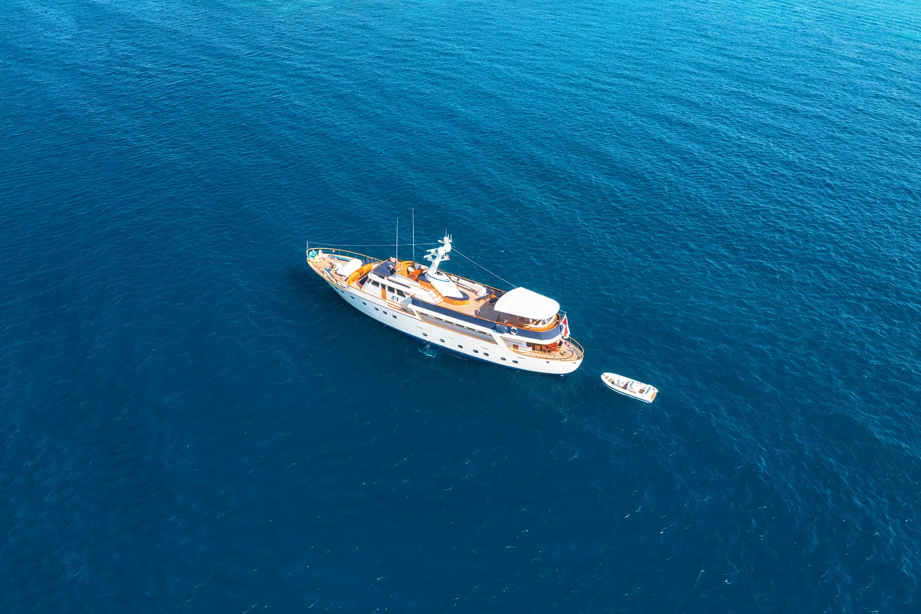 Aerial view of a luxurious yacht sailing on calm, deep blue ocean water, with a smaller tender boat Aerial view of a luxurious yacht sailing on calm, deep blue ocean water, with a smaller tender boat