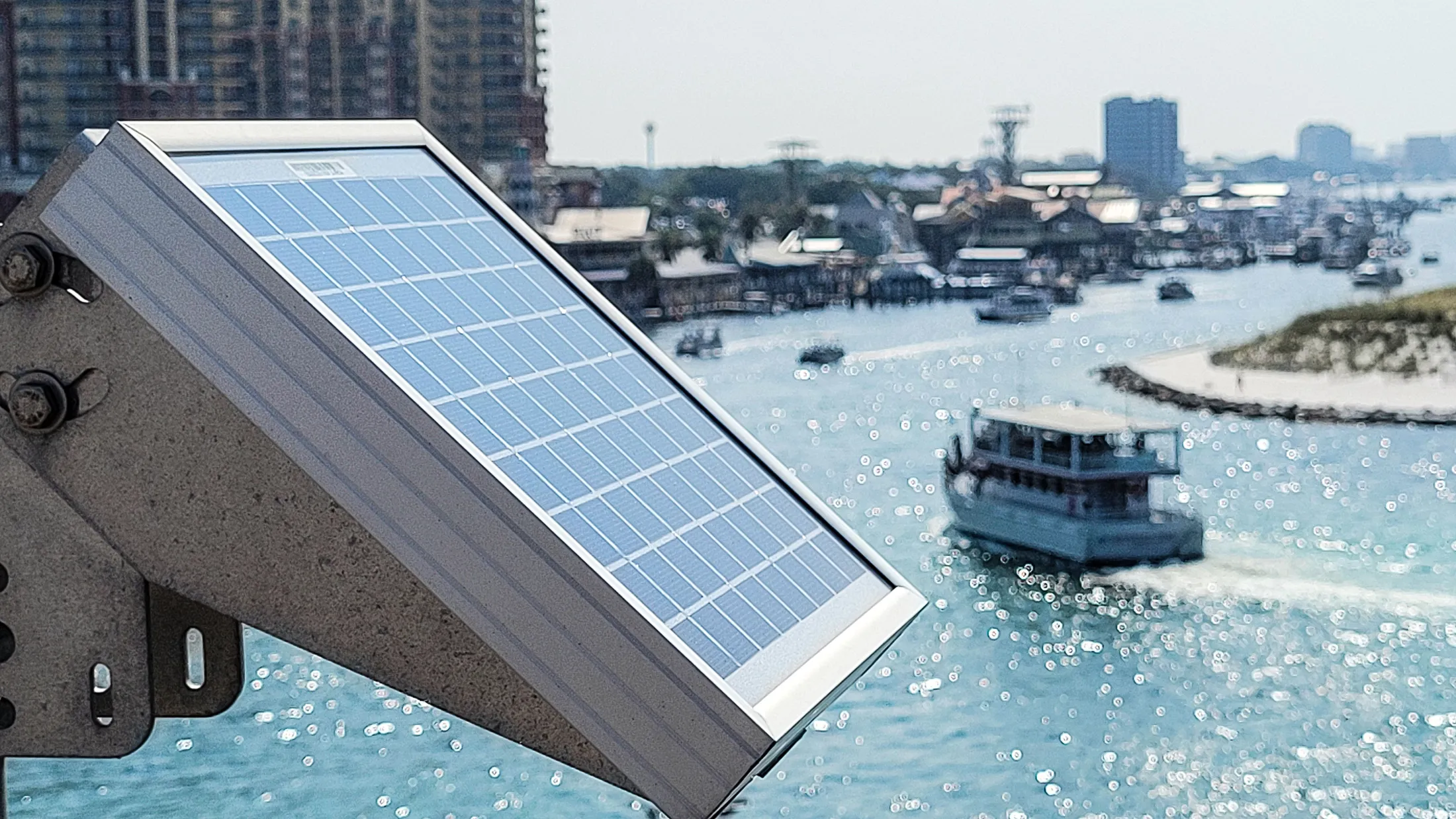 solar-panels-soaking-up-the-sun-at-the-beach-to-po-2025-02-15-18-24-41-utc Solar panel capturing sunlight near a marina with boats on the water, illustrating renewable energy use for marine and coastal applications.